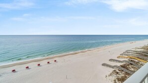 A beach with a clear sky, a sandy shore, and a series of yellow and gray structures along the water's edge. - Windemere 602 (Pensacola)