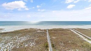 En strand med en lang pir der strækker sig ud i havet, sand og græsklitter.