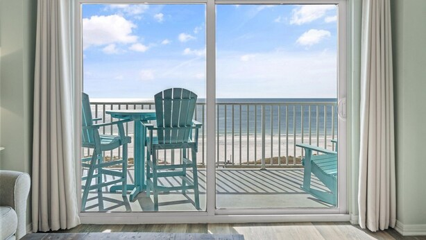 En balkon med udsigt over stranden, et bord og to stole.