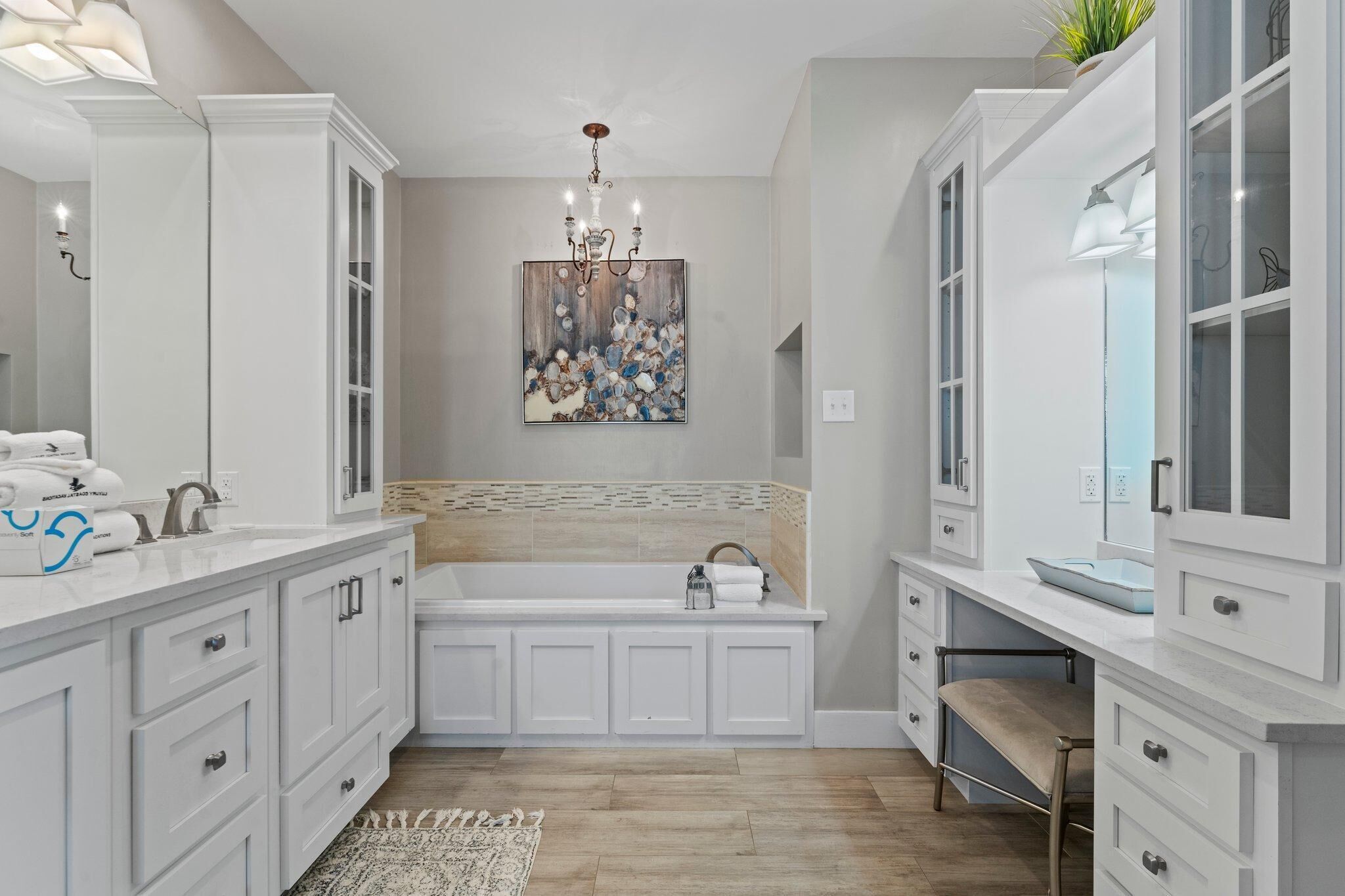 A modern bathroom with white cabinetry, a large mirror, a chandelier, and a decorative wall piece.