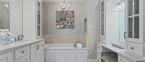 A modern bathroom with white cabinetry, a large mirror, a chandelier, and a decorative wall piece.