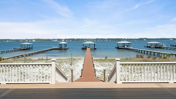 A wooden deck leading to a pier with covered seating areas and a view of the water. - Lime In The Coconut (Gulf Shores)