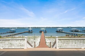 A wooden deck leading to a pier with covered seating areas and a view of the water. - Lime In The Coconut (Gulf Shores)