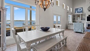 A spacious room with a large dining table, white chairs, and a view of the sea through large windows. - Lime In The Coconut (Gulf Shores)