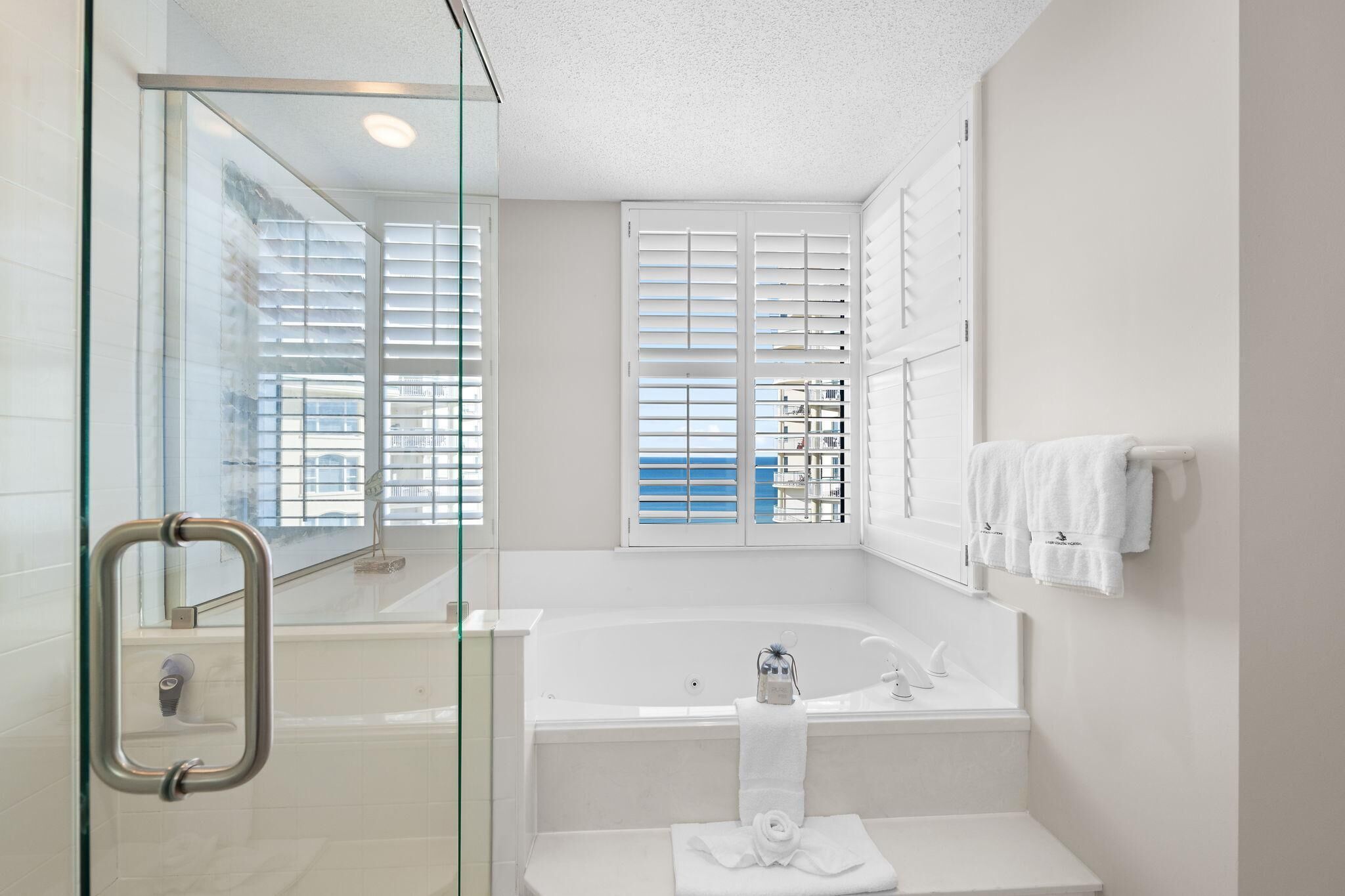 A modern bathroom with a glass shower enclosure, a bathtub, and a window with blinds.