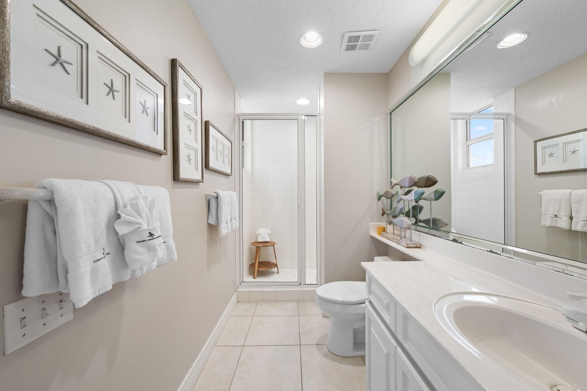 A modern bathroom with a large mirror, white fixtures, and framed artwork on the wall.
