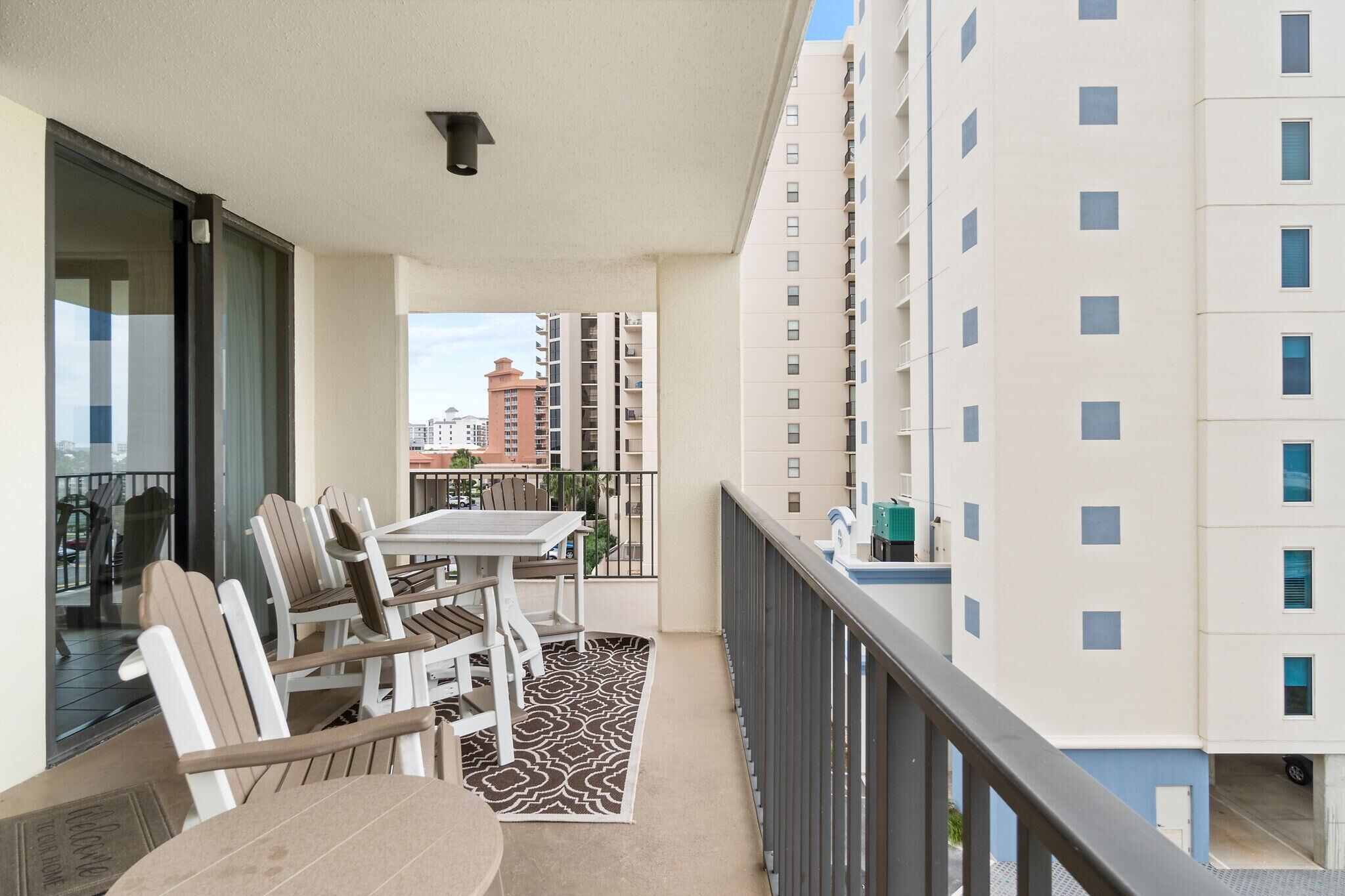 Een balkon met een tafel en stoelen, een kleed met een patroon en een uitzicht op omliggende gebouwen.