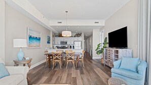 A modern living room with a dining area, a TV, and a kitchen in the background. - Regency Isle Penthouse 1106 (Orange Beach)