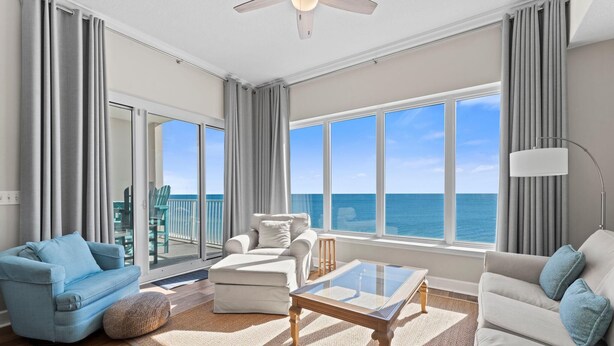 A spacious living room with a large window overlooking the ocean, a ceiling fan, and a modern light fixture. - Regency Isle Penthouse 1106 (Orange Beach)