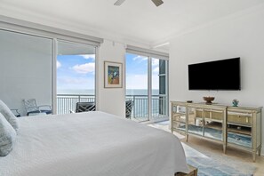 A bedroom with a large bed, a TV mounted on the wall, a balcony with a view of the sea, and a dining area with a table and chairs. - Palacio Penthouse 1902 (Pensacola)