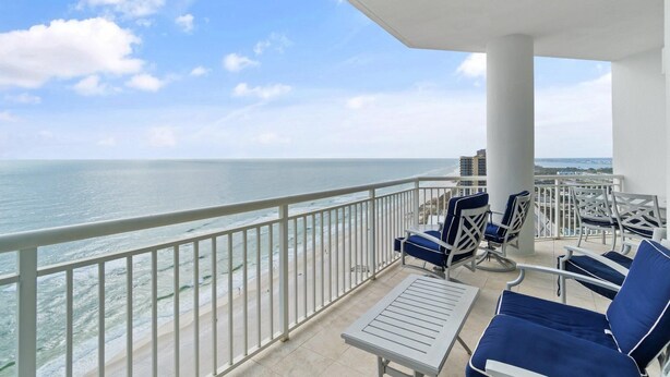 A balcony with white railings, blue cushioned chairs, and a view of the ocean. - Palacio Penthouse 1902 (Pensacola)