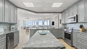 A modern kitchen with grey cabinets, a central island, and a large window overlooking a balcony. - Palacio Penthouse 1902 (Pensacola)