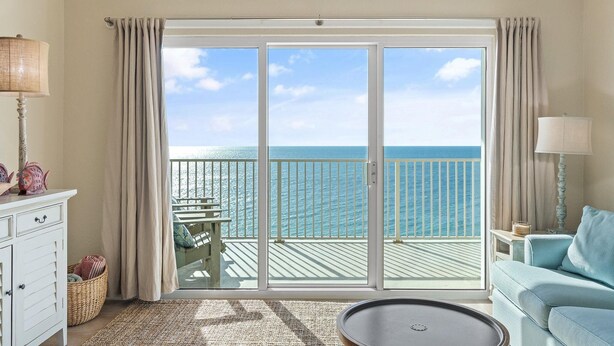 Una habitación con vistas al océano, un balcón con mesa y sillas, un sofá y una lámpara.