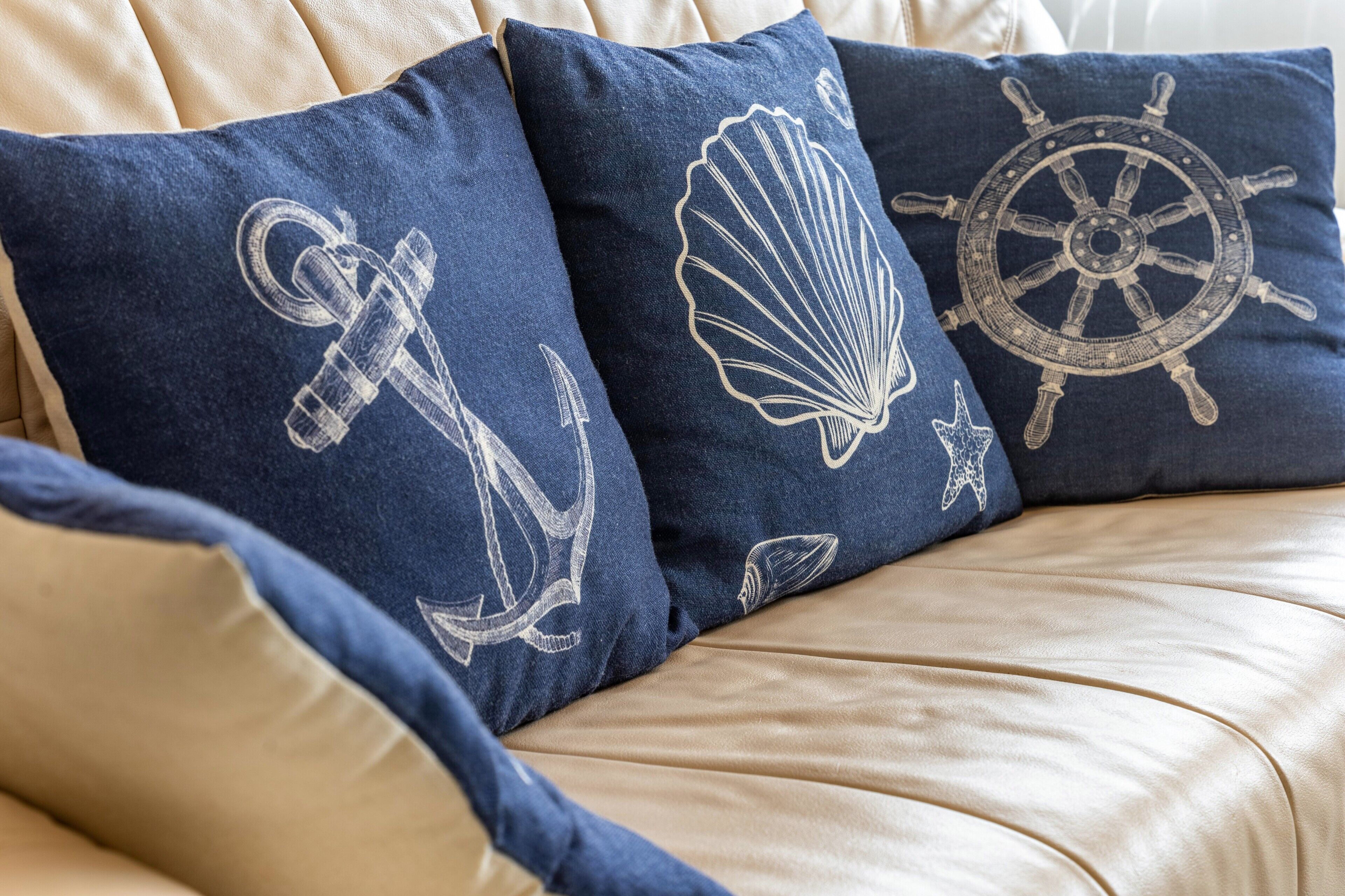 A sofa with three navy blue pillows featuring nautical designs.
