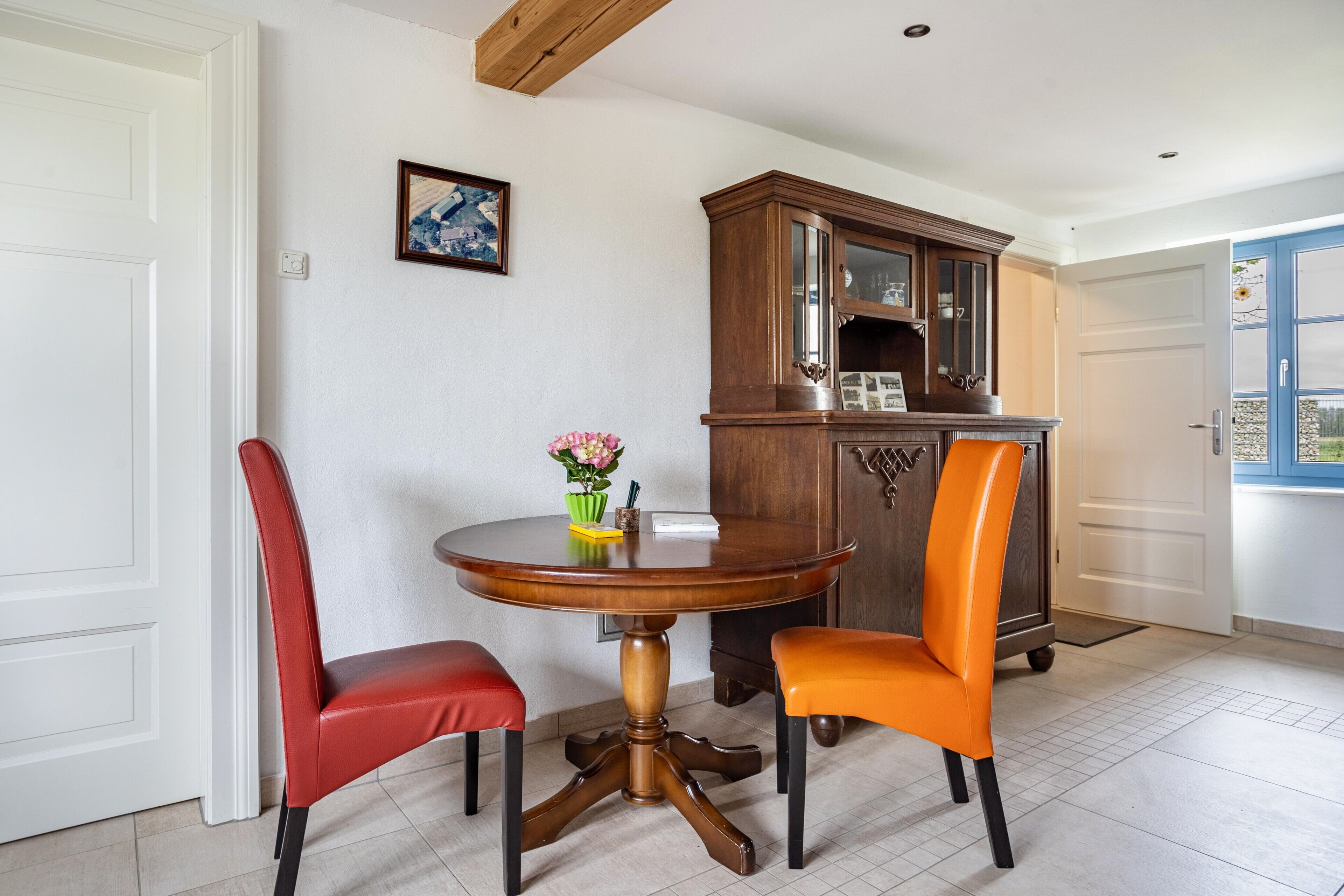 Un coin repas comprenant une table ronde en bois, deux chaises, un buffet et une porte.