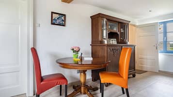 Un coin repas comprenant une table ronde en bois, deux chaises, un buffet et une porte.