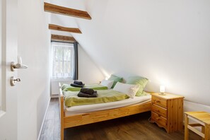 A single bed with a wooden headboard, a bedside table with a lamp, and a window with a view of greenery. - Apartment 'Kornkammer' with Lake View, Private Garden and Wi-Fi (Usedom)