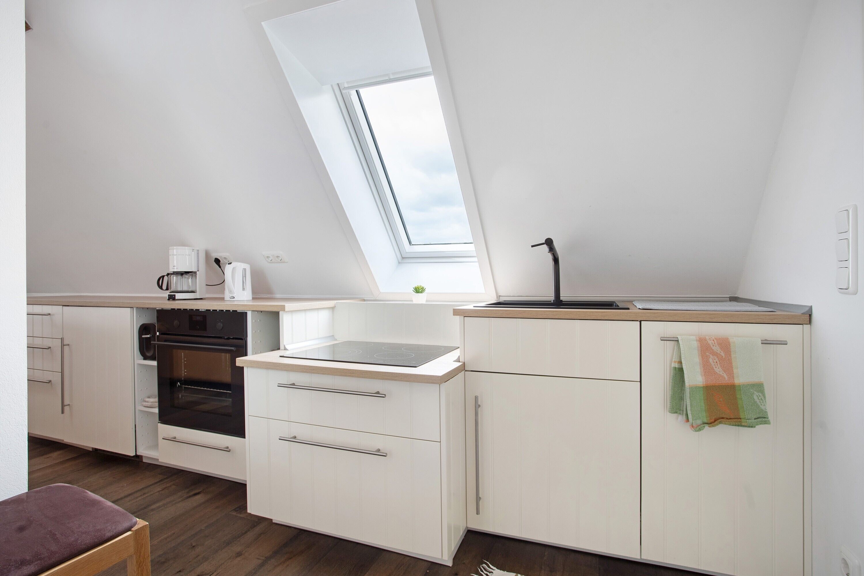 Une cuisine moderne dotée d’un puits de lumière, d’un four encastré et de meubles de rangement blancs.