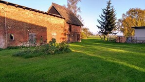 Een landelijk, stenen gebouw met rieten dak, omgeven door een verzorgd gazon en bomen.