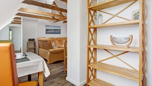 Een kamer met een houten plafond, een bank, een tafel met een witte tafelkleed en een houten plank met glazen flessen.