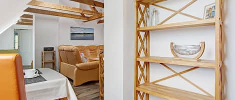 A room with a wooden ceiling, a sofa, a table with a white tablecloth, and a wooden shelf with glass bottles.