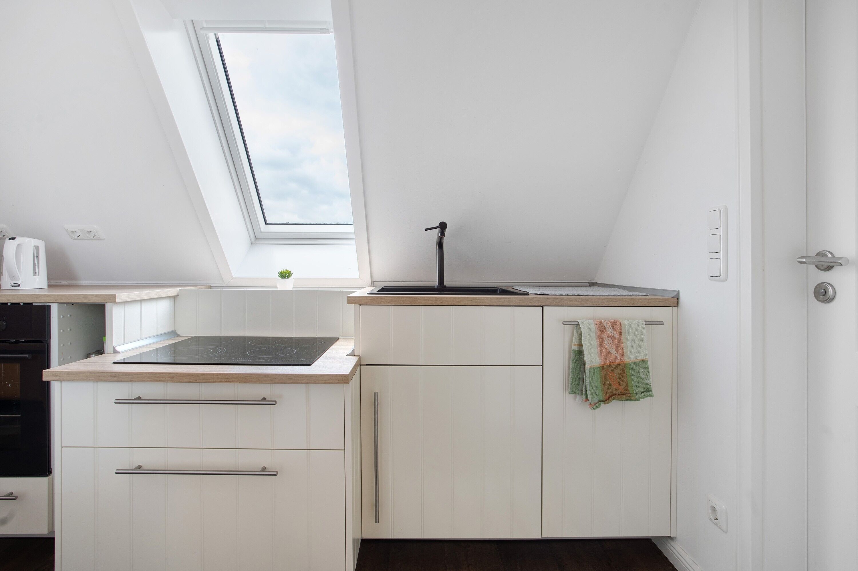 Une cuisine dotée d’une lucarne, de meubles blancs, d’un robinet noir et d’une serviette accrochée à la porte.