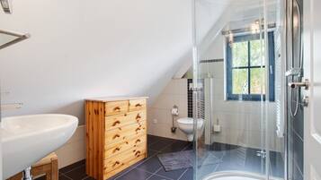 Et moderne badeværelse med en glasvæg omkring brusebad, et træskab, en hvid vask og et vindue med udsigt.