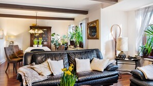 A living room with a black leather sofa, a dining area with a table and chairs, and a kitchen area with a stove. - Holiday Home 'Elbparadies' with Private Terrace and Wi-Fi (Stade)