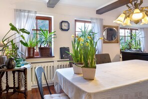 Ein Essbereich mit Tisch, Stühlen, Topfpflanzen, einer Uhr und einem Fenster mit Vorhängen.