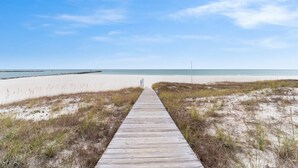Eine Holzpromenade, die zu einem Strand mit blauem Himmel führt.