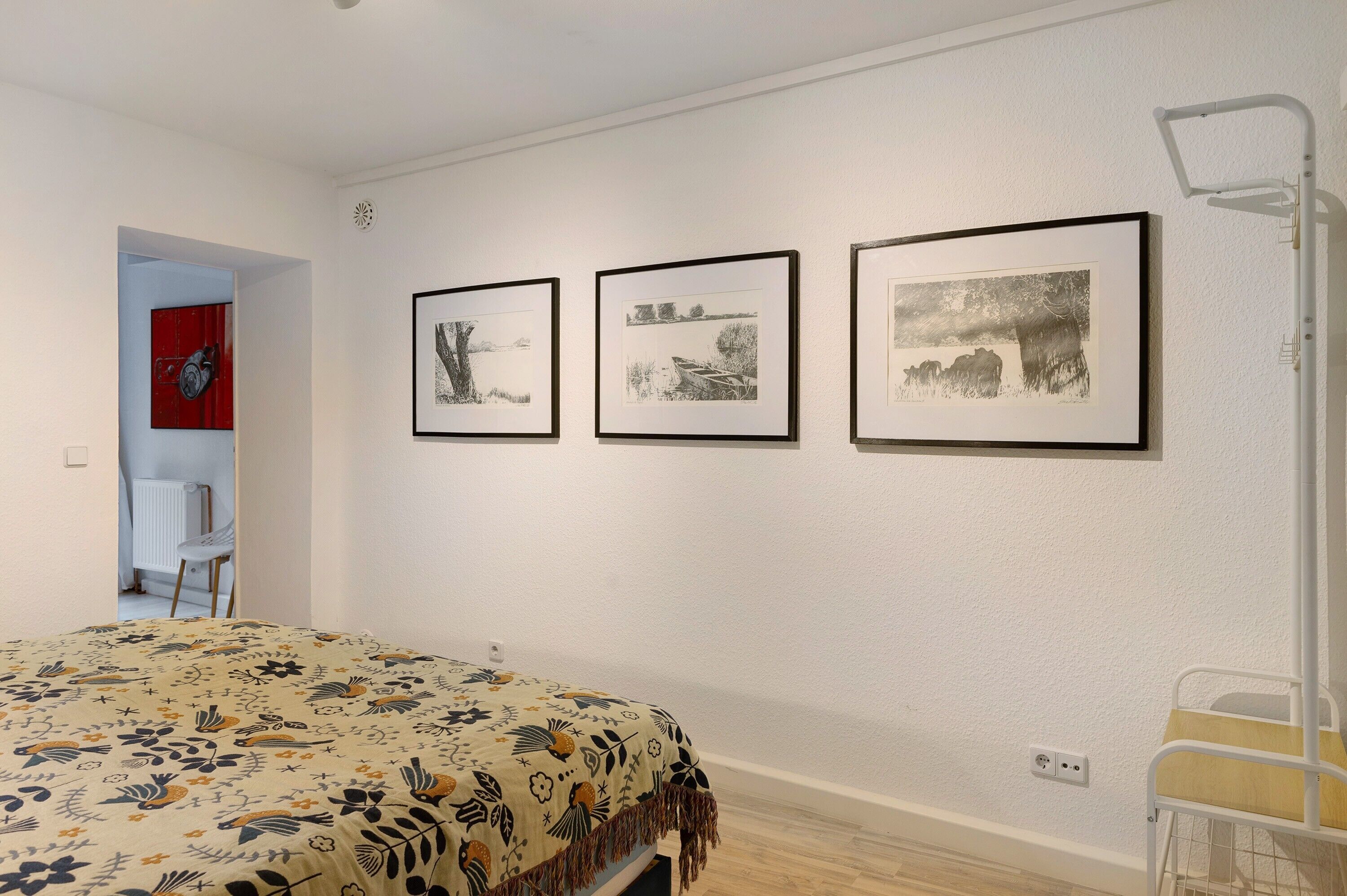 A bedroom with a bed, a chair, and three framed pictures on the wall.