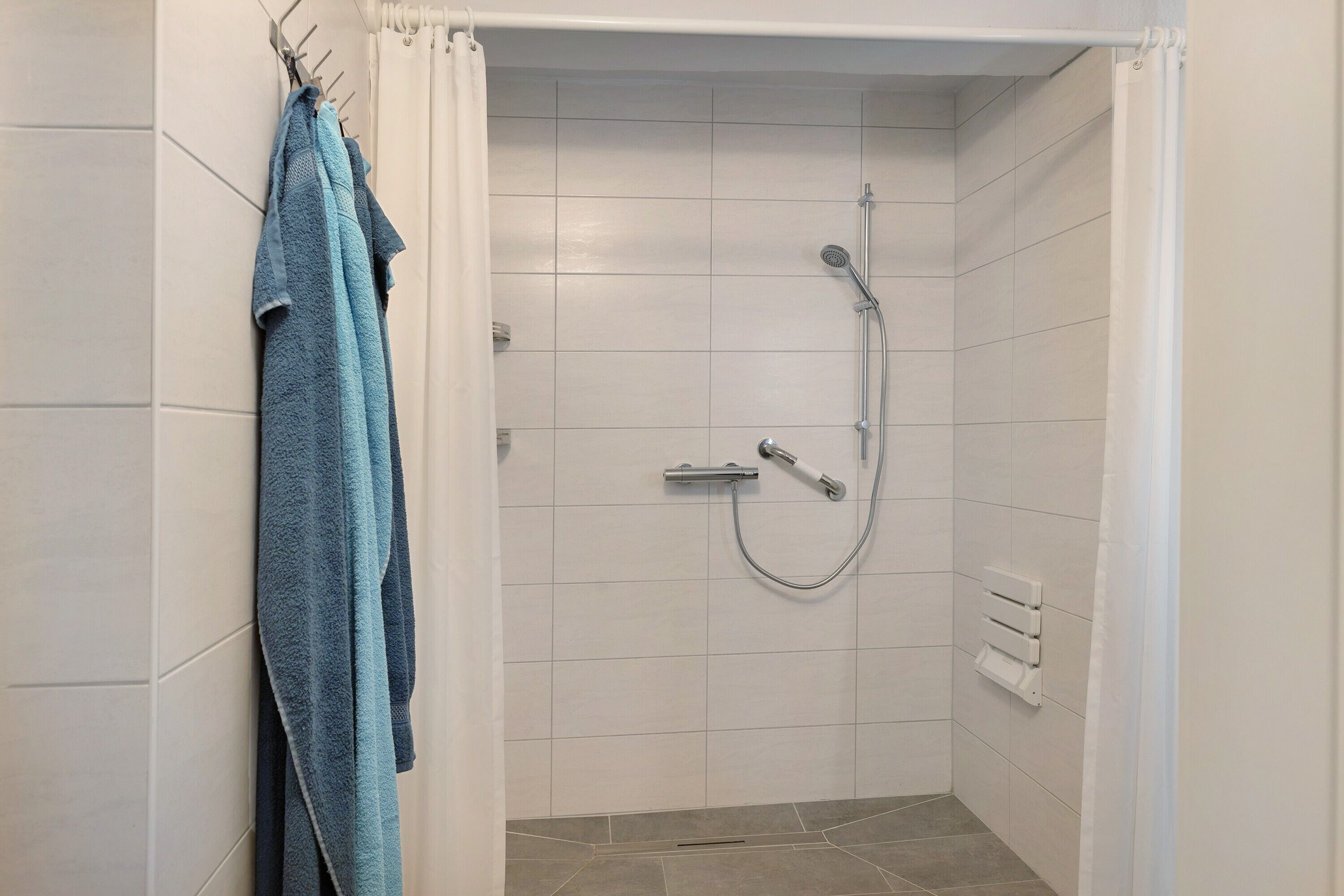 A small, tiled shower room with a showerhead and control panel.