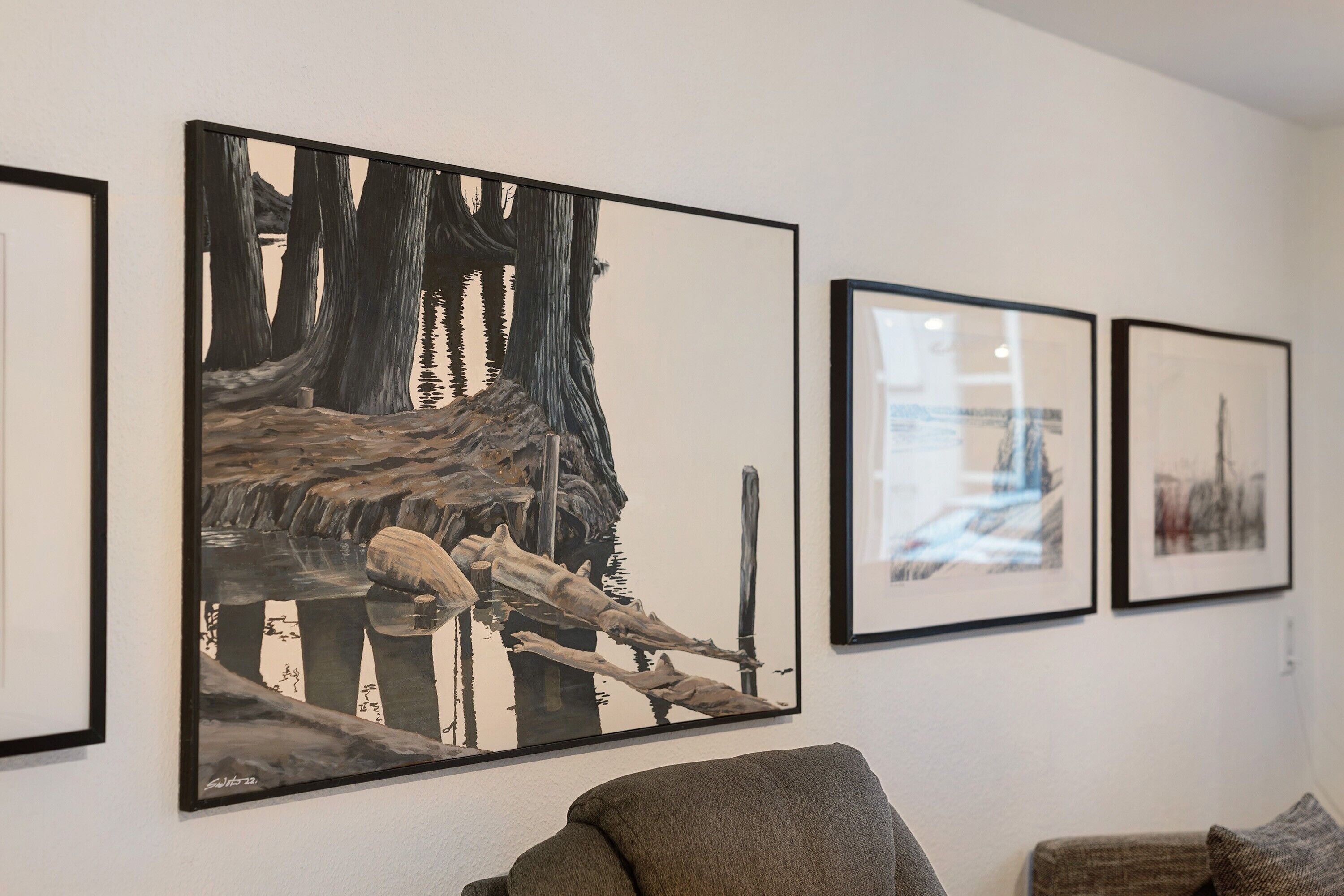 Een kamer met een groot kunstwerk in een lijst, waarop een natuurscène te zien is, een bank en een kleiner fotokader aan de muur.