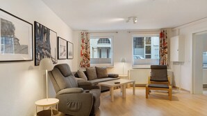 Uma sala de estar moderna com sofá, poltrona e mesa de centro, com obras de arte nas paredes e grandes janelas.