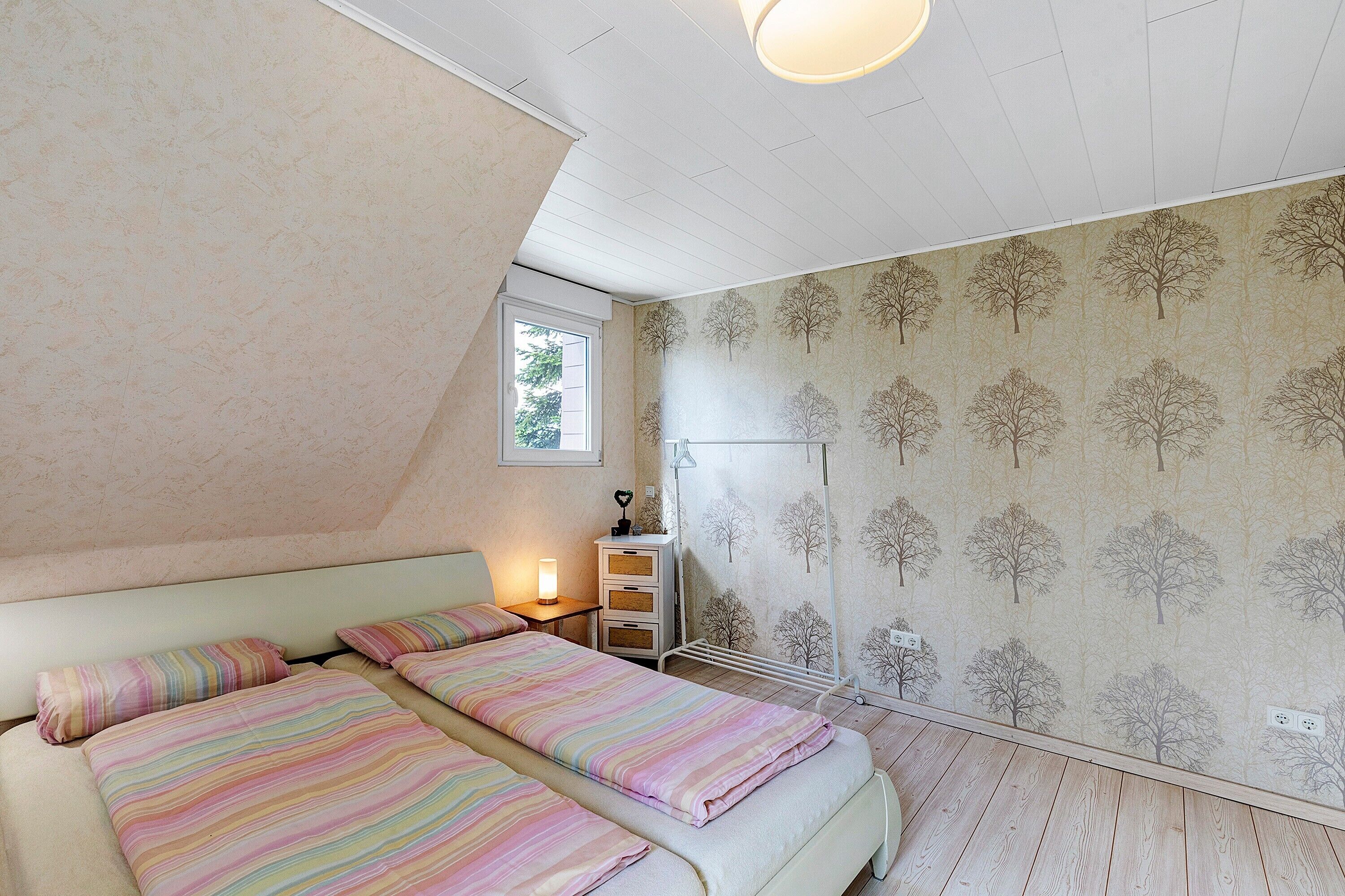 Une chambre avec deux lits, une fenêtre, une table de chevet avec une lampe et un radiateur.