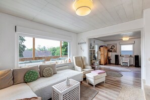 Uma sala de estar ampla com uma janela grande, um sofá, uma poltrona e uma mesinha.