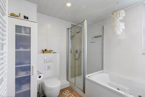 Uma casa de banho moderna com chuveiro em cabine de vidro, banheira branca e sanita.