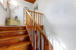 Un escalier en bois avec une rampe, une commode décorée de motifs en forme de cœur et une lanterne fixée au mur.