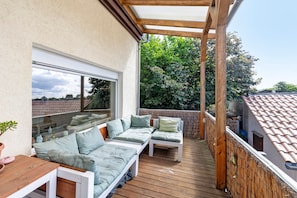 Un espace extérieur abrité, aménagé avec du mobilier en bois et offrant une vue sur le paysage urbain.