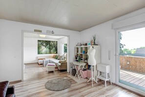 Un salon comprenant un canapé, une table basse et une bibliothèque. Une grande fenêtre offre une vue sur l’extérieur.