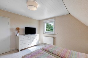Une chambre avec une commode blanche, une télévision, une fenêtre donnant sur un beau paysage et deux lits.