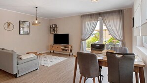 Una sala de estar con sofá, televisor, mesa de comedor, sillas y lámpara de techo.