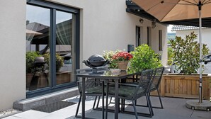 Un patio al aire libre con una mesa, sillas, una parrilla y un gran paraguas.