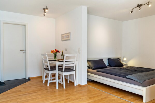 Une pièce de taille modeste comprenant un lit, une table à manger avec des chaises et une petite table sur laquelle sont posés un vase et une bouteille.