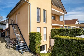 Un immeuble à plusieurs étages, doté d’un escalier, d’un balcon et d’une haie.