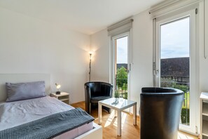 Une chambre à coucher avec un lit, une chaise, une table et une grande fenêtre.