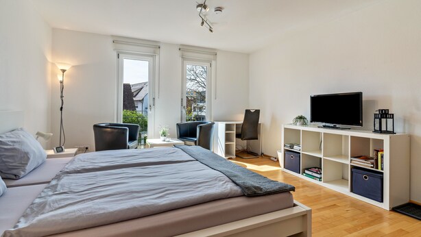 Une chambre à coucher comprenant un lit, des tables de chevet, un bureau, une chaise, une télévision et une bibliothèque.