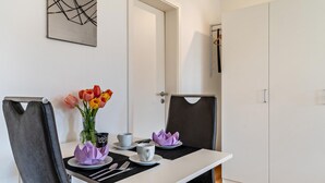 Un coin repas avec une table dressée pour deux personnes, un vase rempli de fleurs et un porte-manteau.