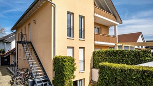 Un immeuble à plusieurs étages, doté d’un escalier, d’un balcon et d’une haie.