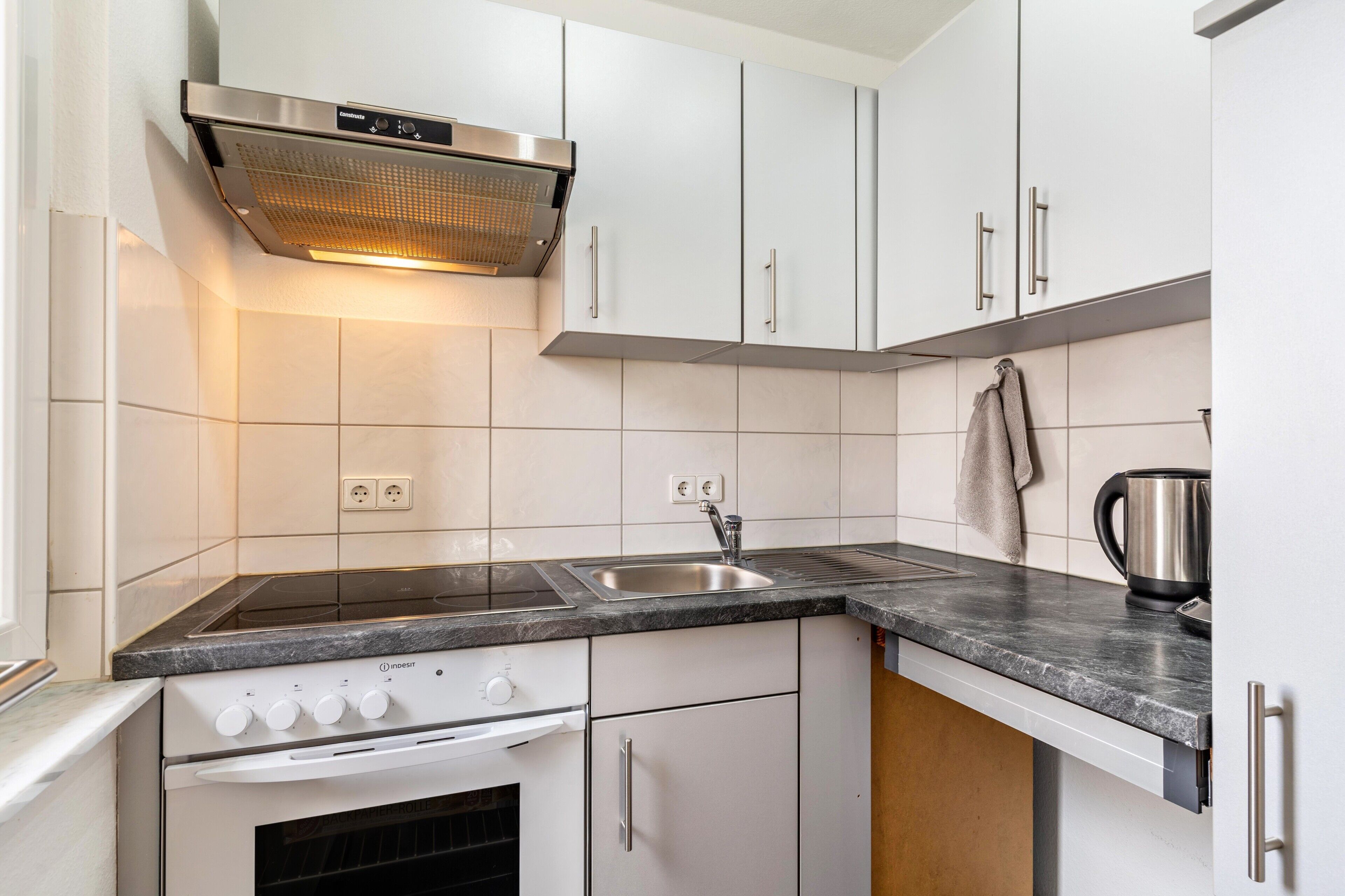 A modern kitchen with white cabinets, a stainless steel range hood, a double sink, and a built-in oven.